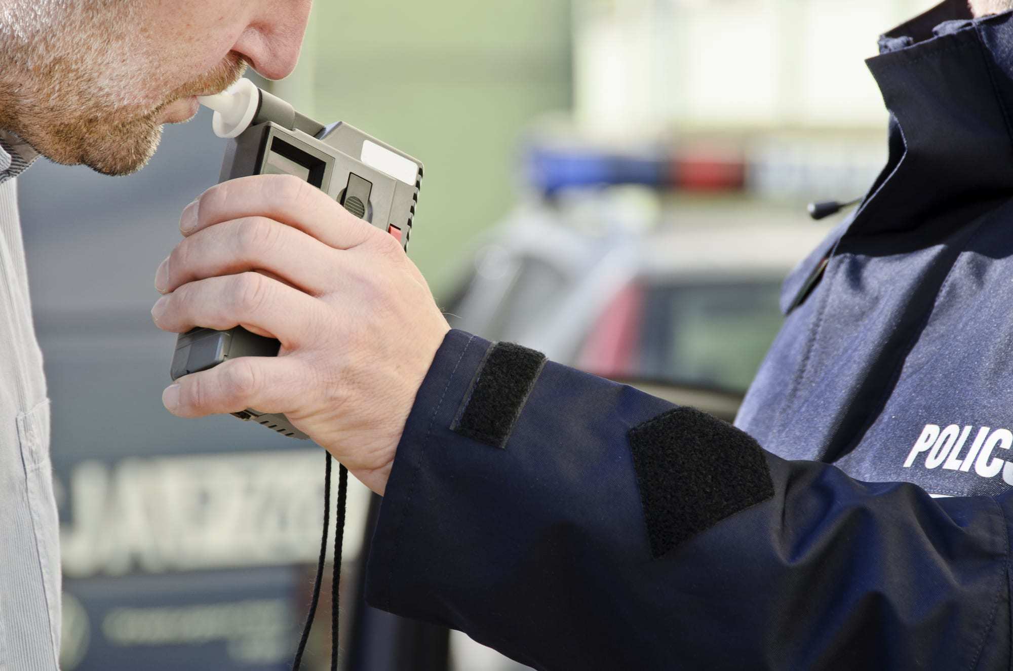 Close-up-of-man-blowing-into-breathalizer-held-up-by-policeman