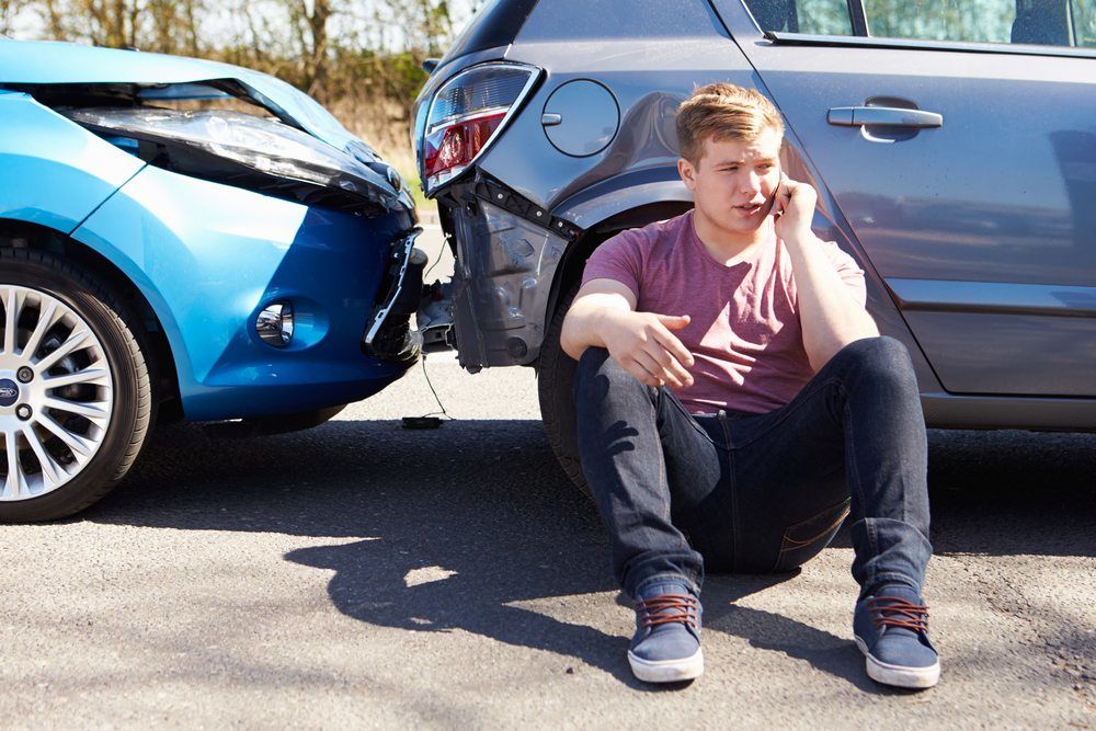 man sitting on ground beside car crash