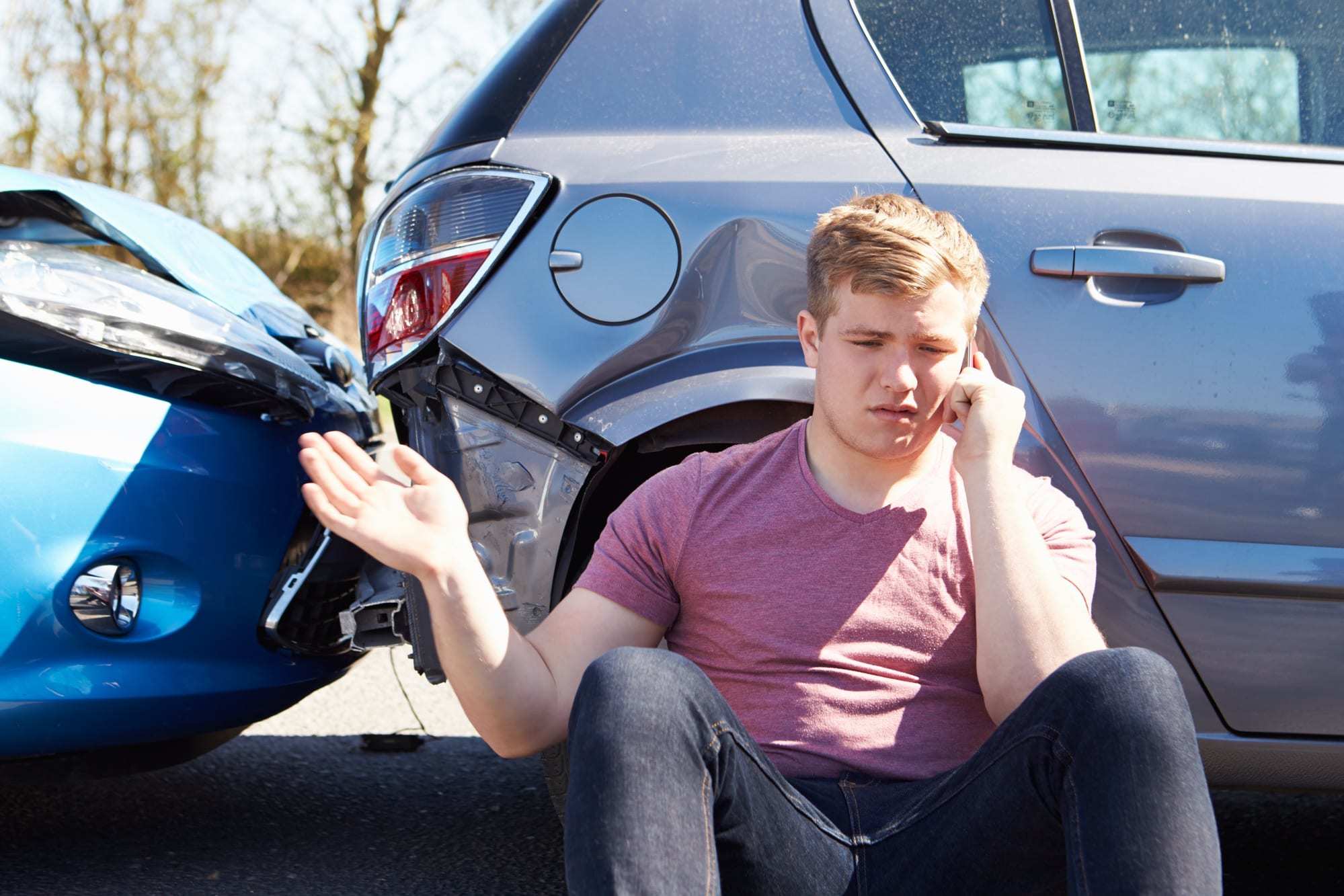 young man sitting on ground beside car accident