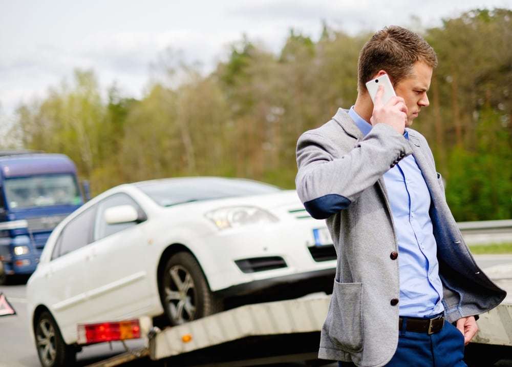 Man calling while tow truck picking up his broken car