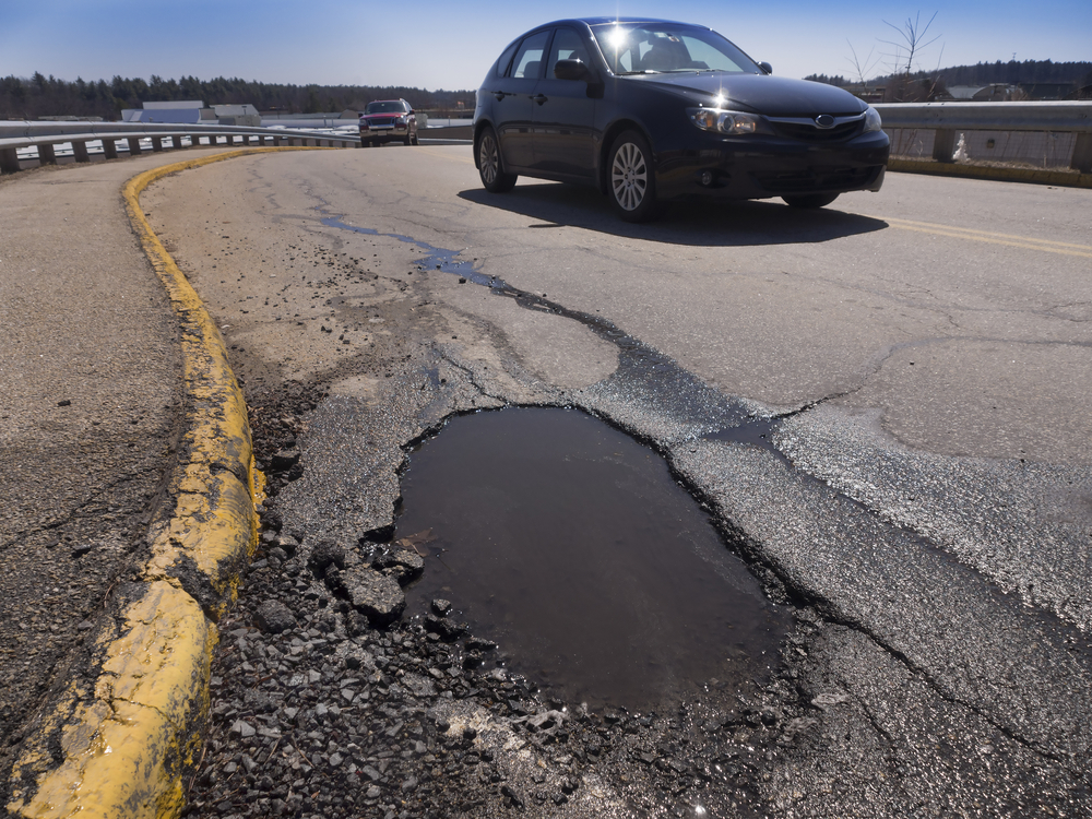 pothole in road, car in background