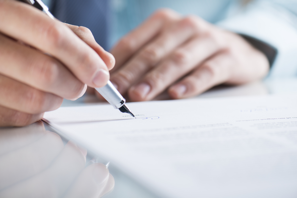 Close-up of hand signing paper with pen