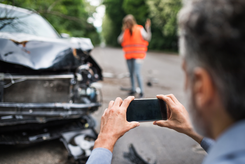 Man taking a photo of car accident damage using cell phone