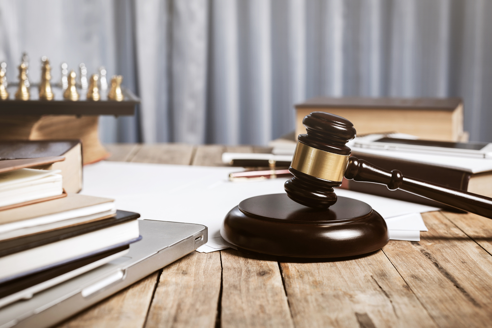 Gavel sitting on wood desk beside laptop, books, chess set, pens