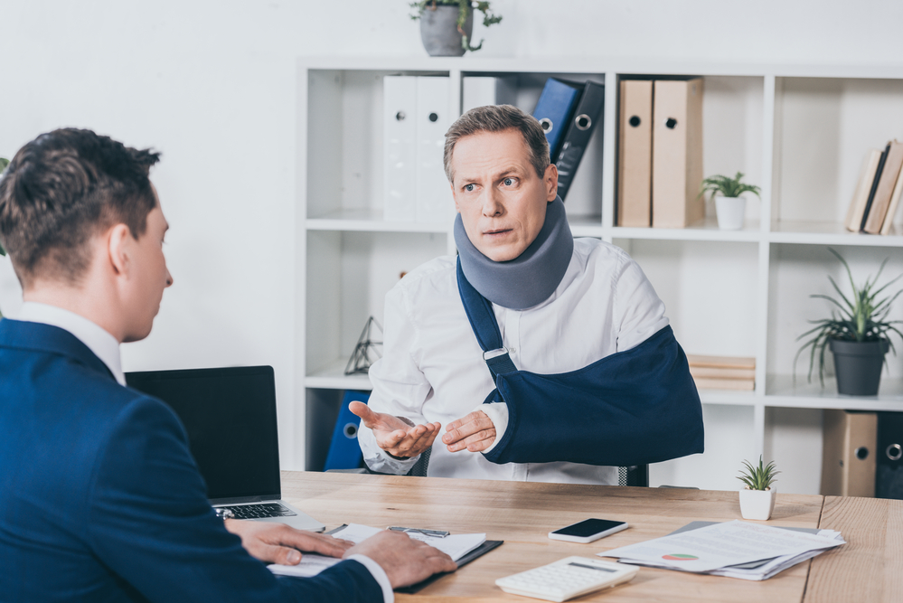 Man with arm in sling talking to another man over desk