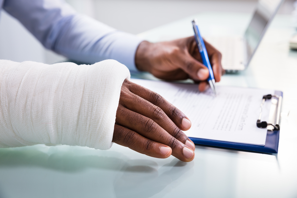 Man with cast on arm signing form on clipboard