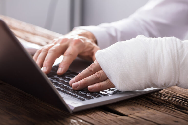 Close-up of businessperson typing on computer with one hand in cast