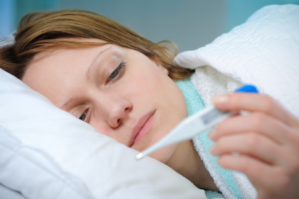 Woman looking at thermometer in bed