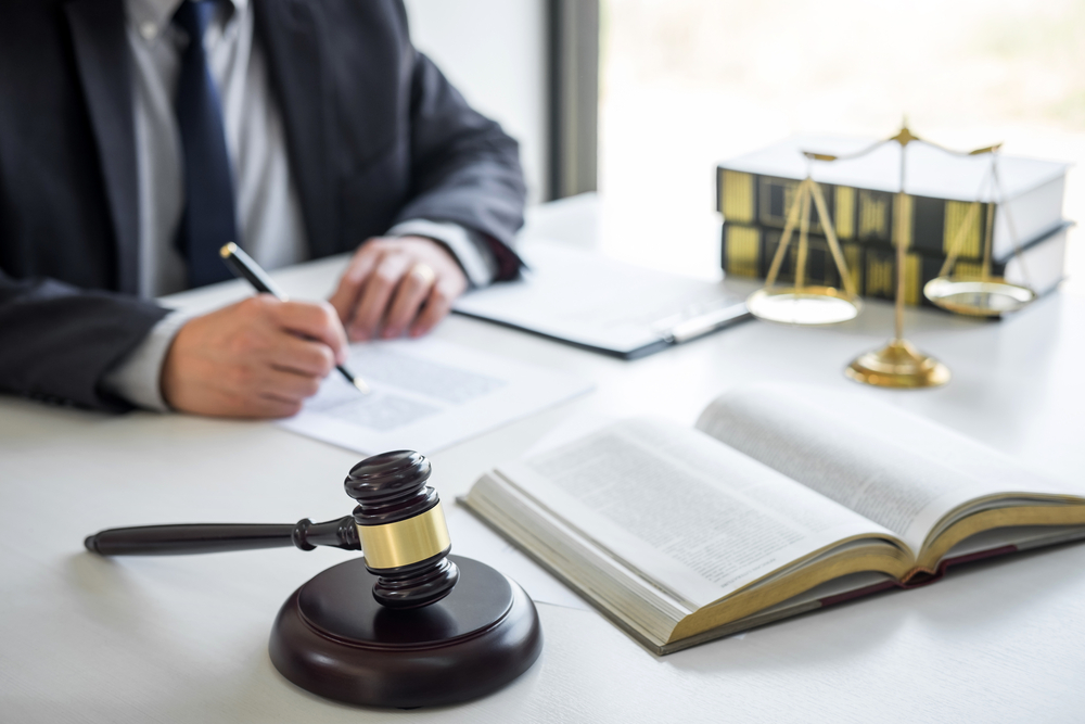 Close-up of attorney at desk, writing, open book, gavel