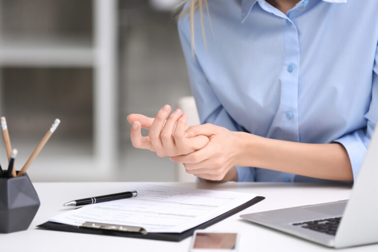 Close-up of young professional woman holding wrist while sitting at desk
