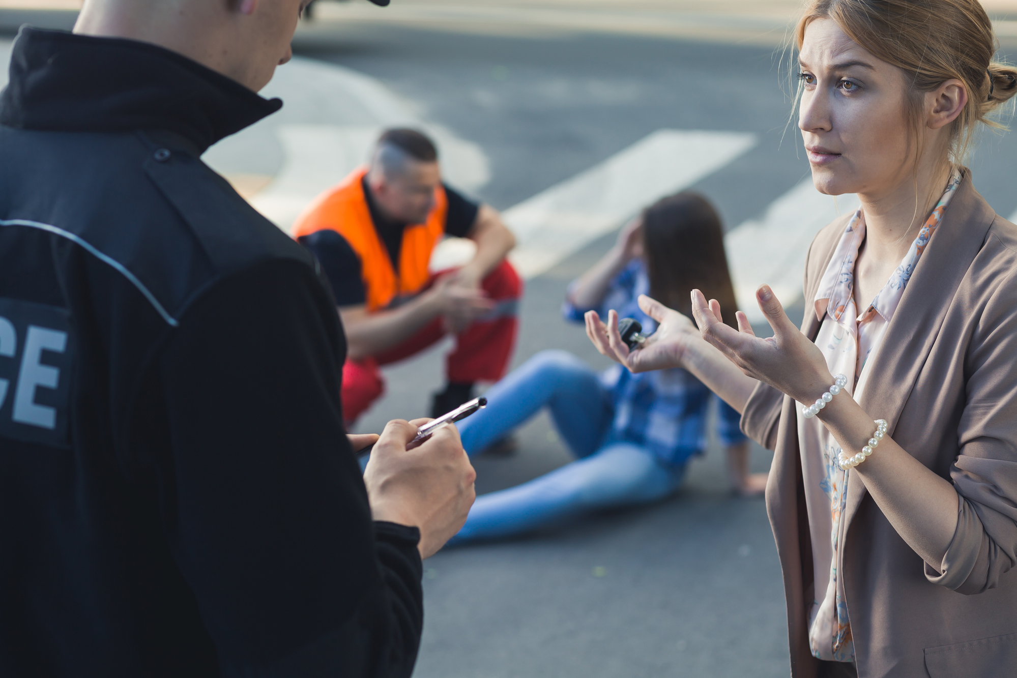 Woman talking to policeman, in background injured woman on ground being helped by professional