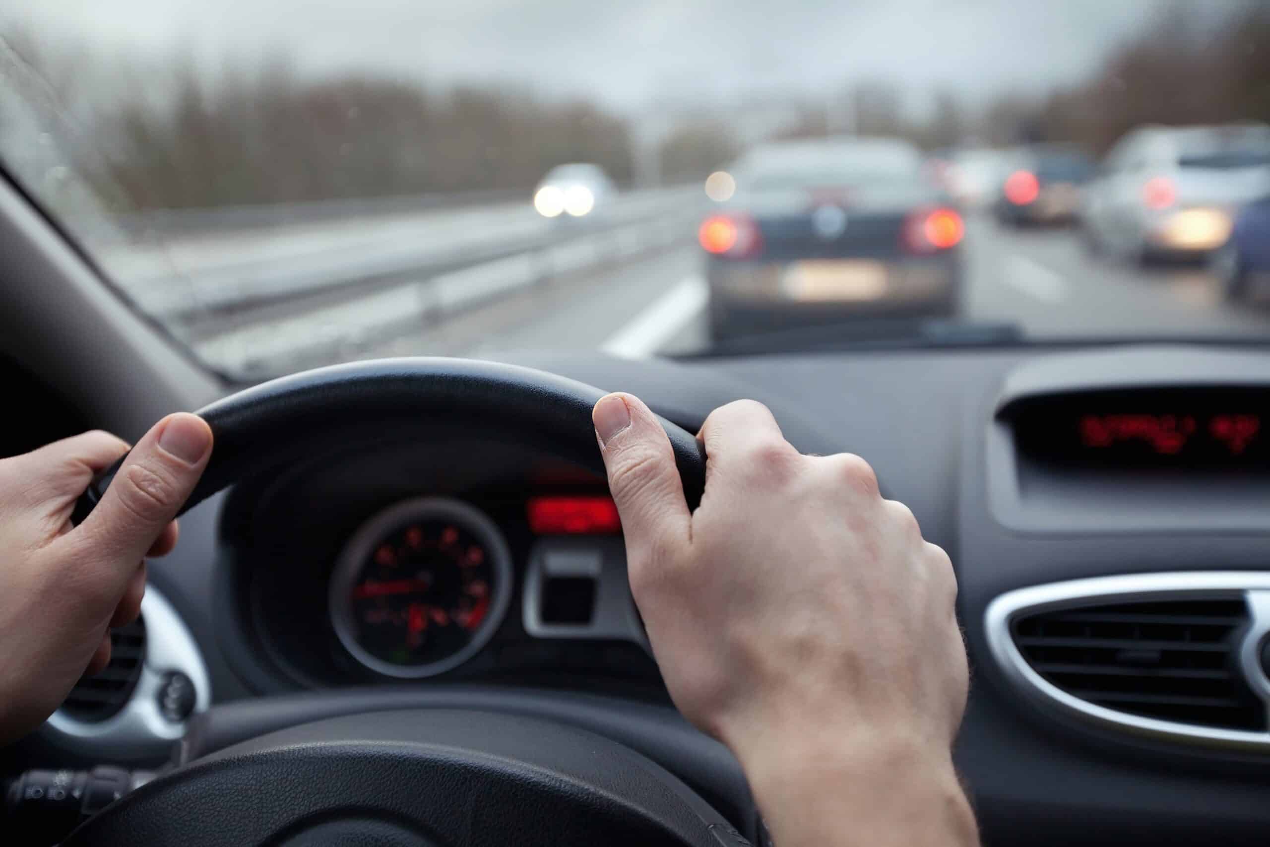 Close-up of hands on steering wheel, other cars visible out window