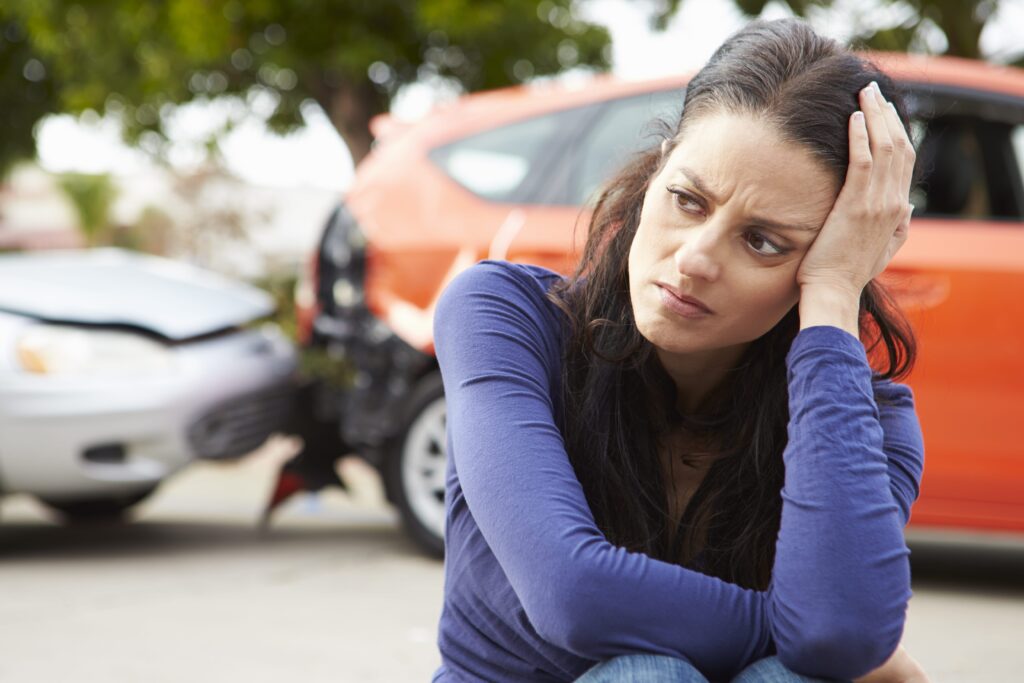 Women holding head, car accident scene behind her