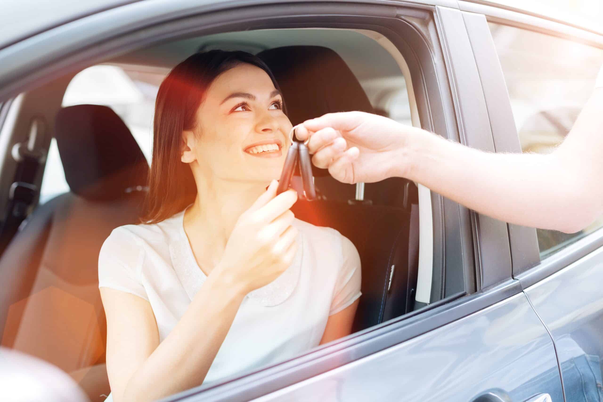 Person handing car keys through open window to young woman driver