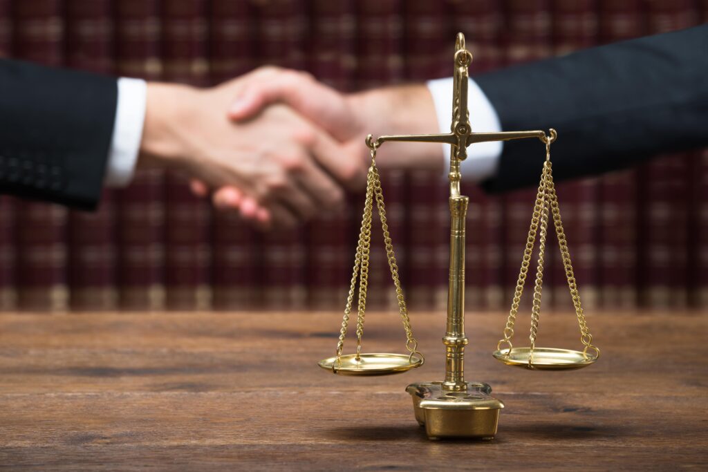 Two professionals shaking hands behind scales of justice