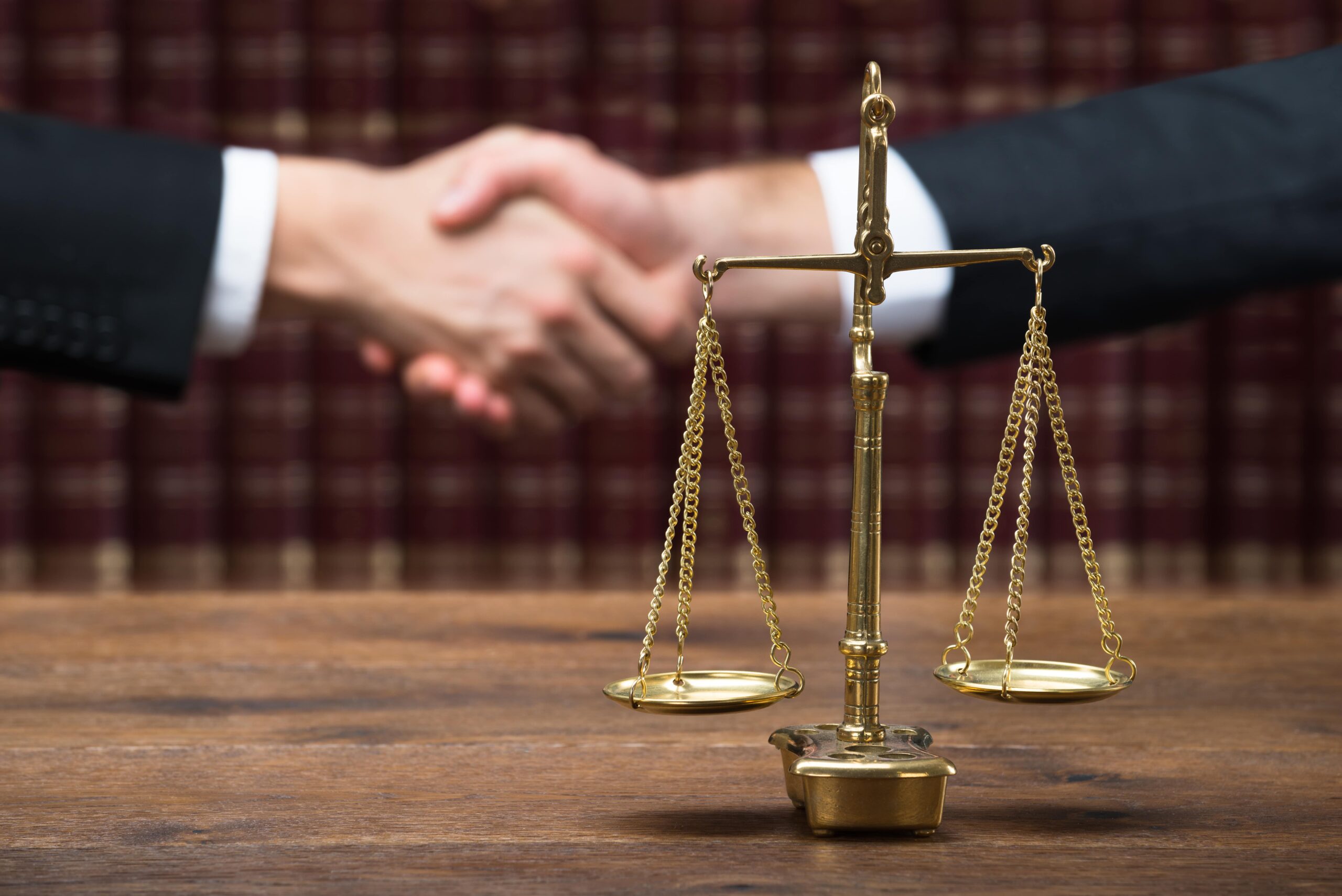Two professionals shaking hands behind scales of justice