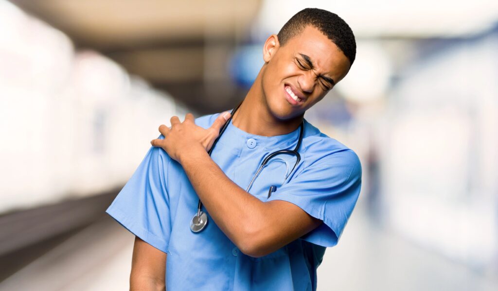 Male nurse grimacing in pain, holding shoulder