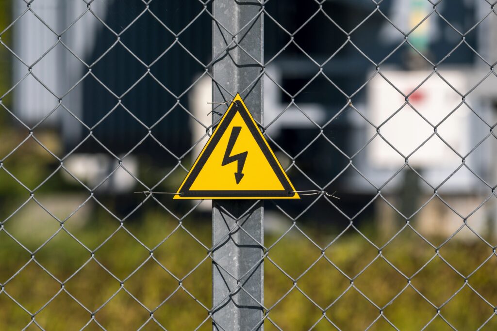 Yellow triangle lightning sign on chain-link fence