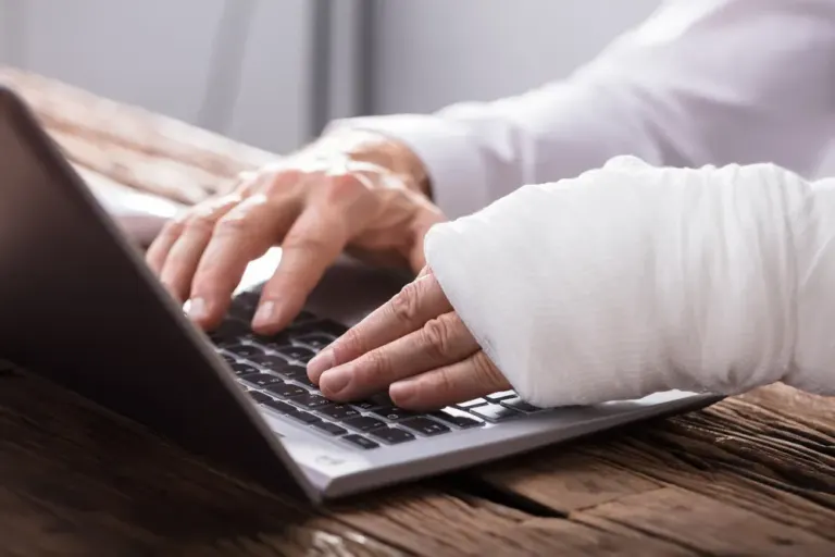 Close-up of businessperson typing on computer with one hand in cast