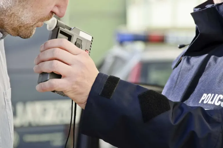 Close-up of man blowing into breathalyzer held up by policeman