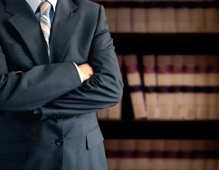 lawyer wearing suit, arms crossed, in front of a bookcase
