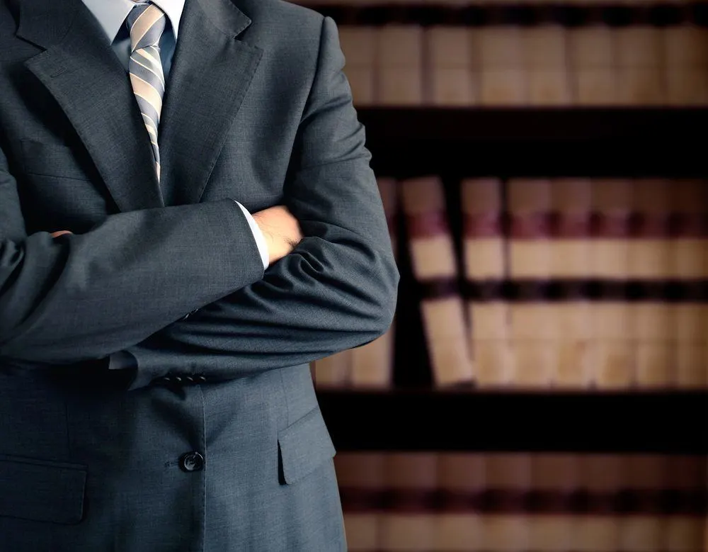 lawyer wearing suit, arms crossed, in front of a bookcase