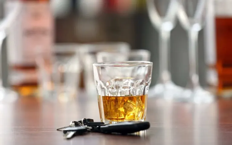 Glass of alcohol and car keys on wooden table