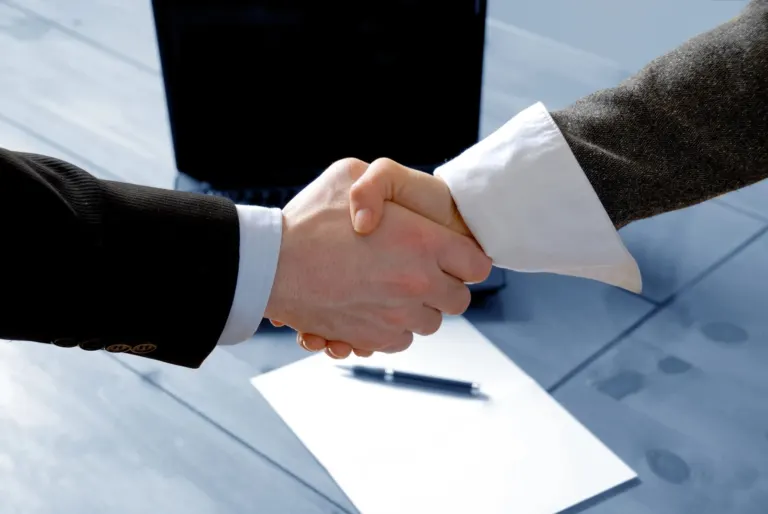 Shaking hands above paper and pen