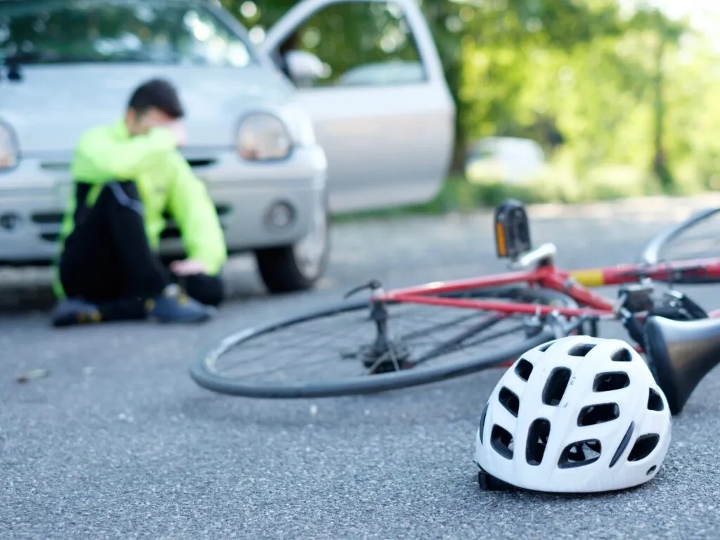 Man on road after an accident, sitting beside bike, helmet, and car